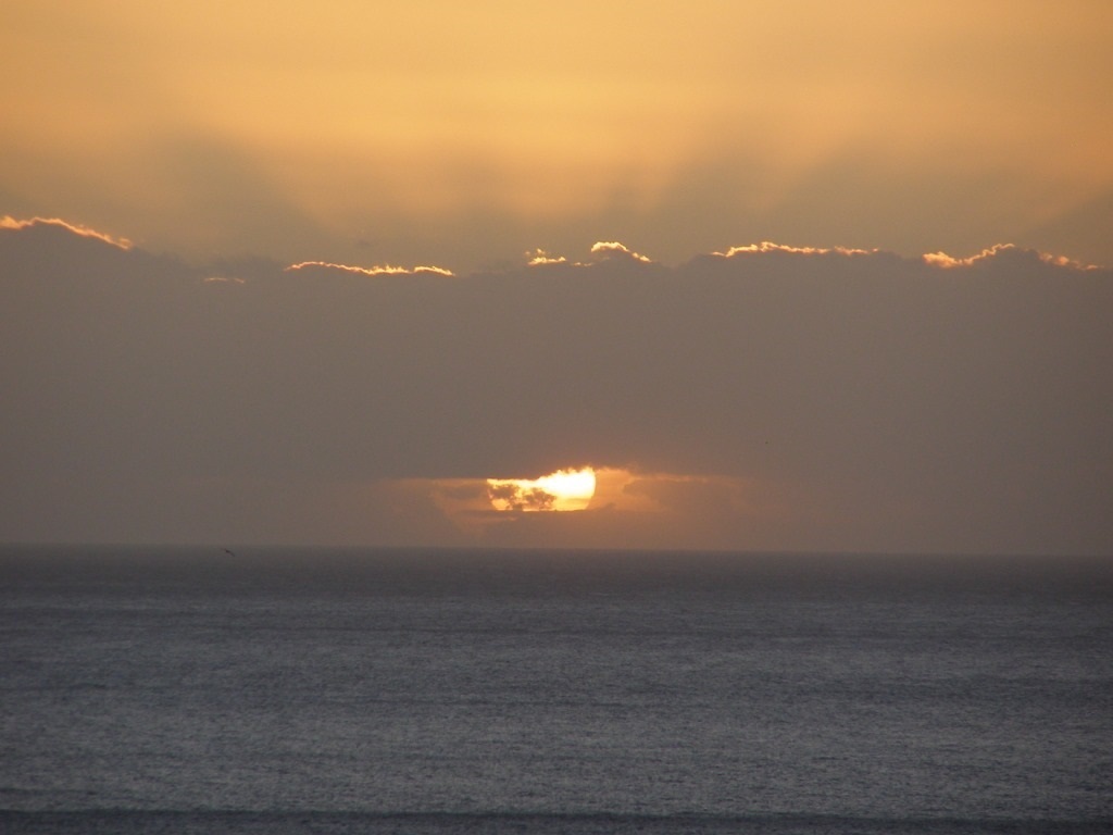Sea sunset with low clouds, the Sun as God partly visible below the clouds, whilst light rays flash forth into the upper sky