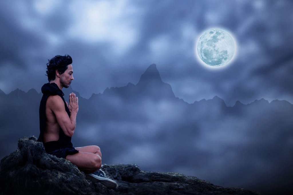 Mystical man on a mountain top meditating under a full moon