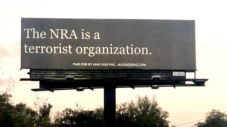 A huge triangular roadside advertising post. On the side that we can see it says 'The NRA is a terrorist organization'.