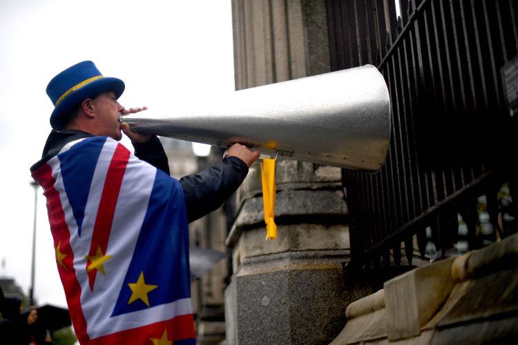 Steve Bray directs a huge metallic megaphone (a bullhorn) at the UK's Houses of Parliament