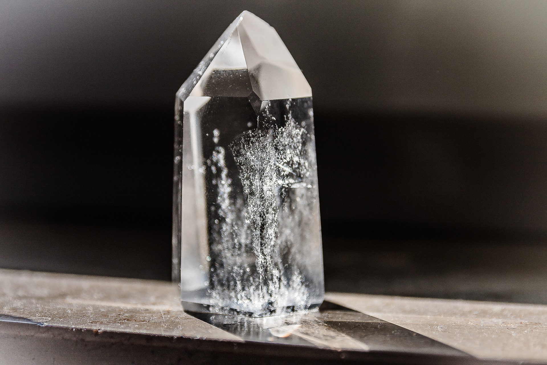 A very clear quartz crystal is sunlit and standing on a dark surface