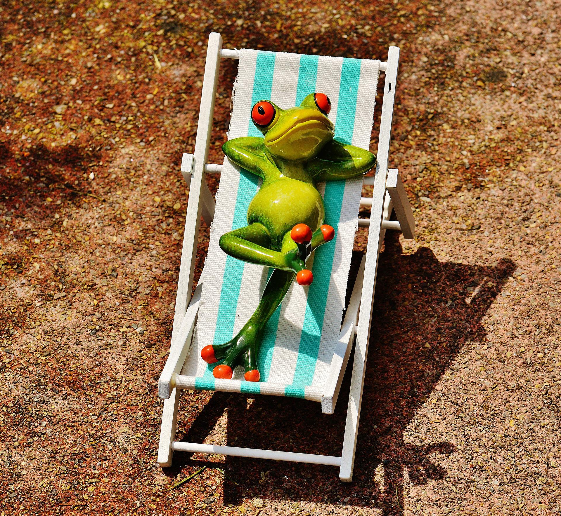 A model frog is relaxing on a deckchair in the sun. Frog's hands crossed behind head, absorbing the sun's rays.