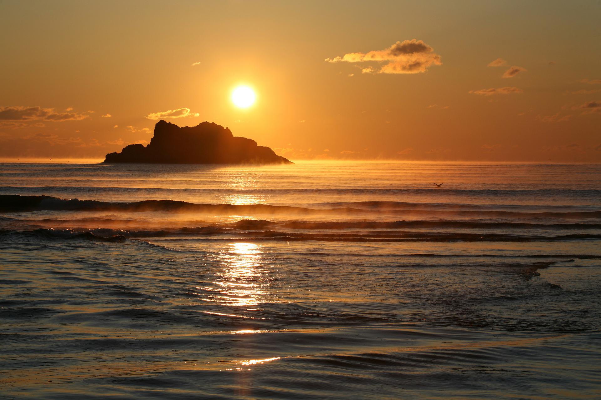 A sunrise from a beach, with a small island only a short swim away