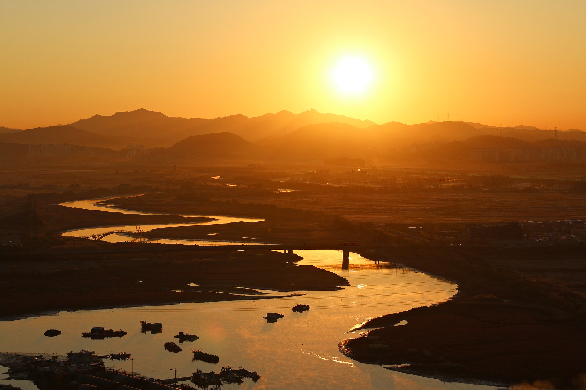 A huge sun is rising or setting in the mountain background; from there, a meandering river weaves its way towards us, getting ever wider