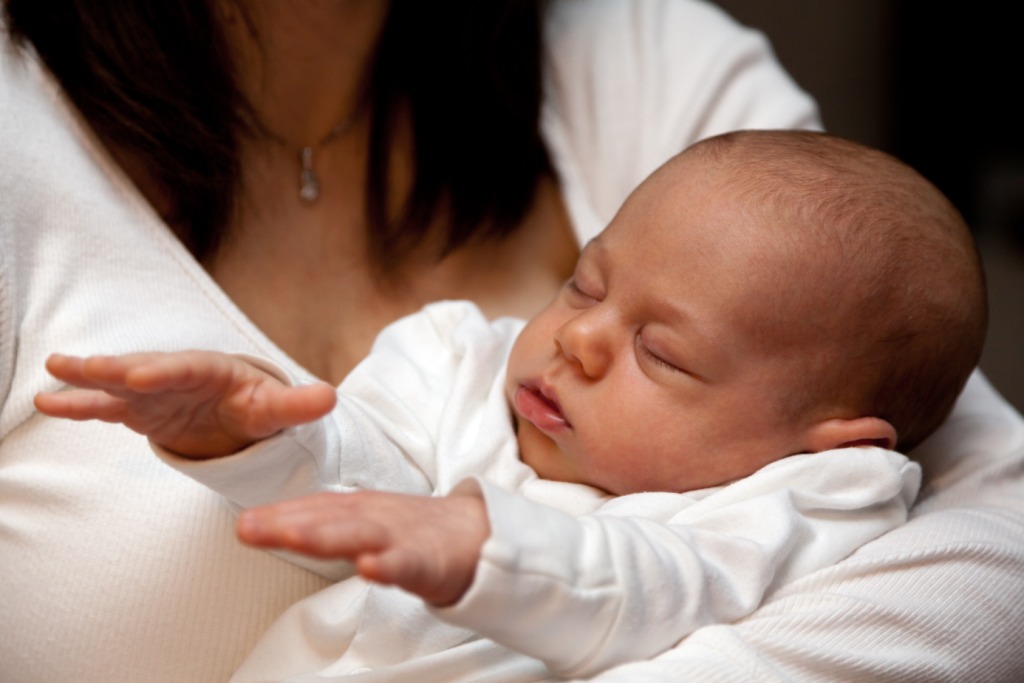 Baby held by mum, calm, eyes closed, hands outstretched, as if healing intensely