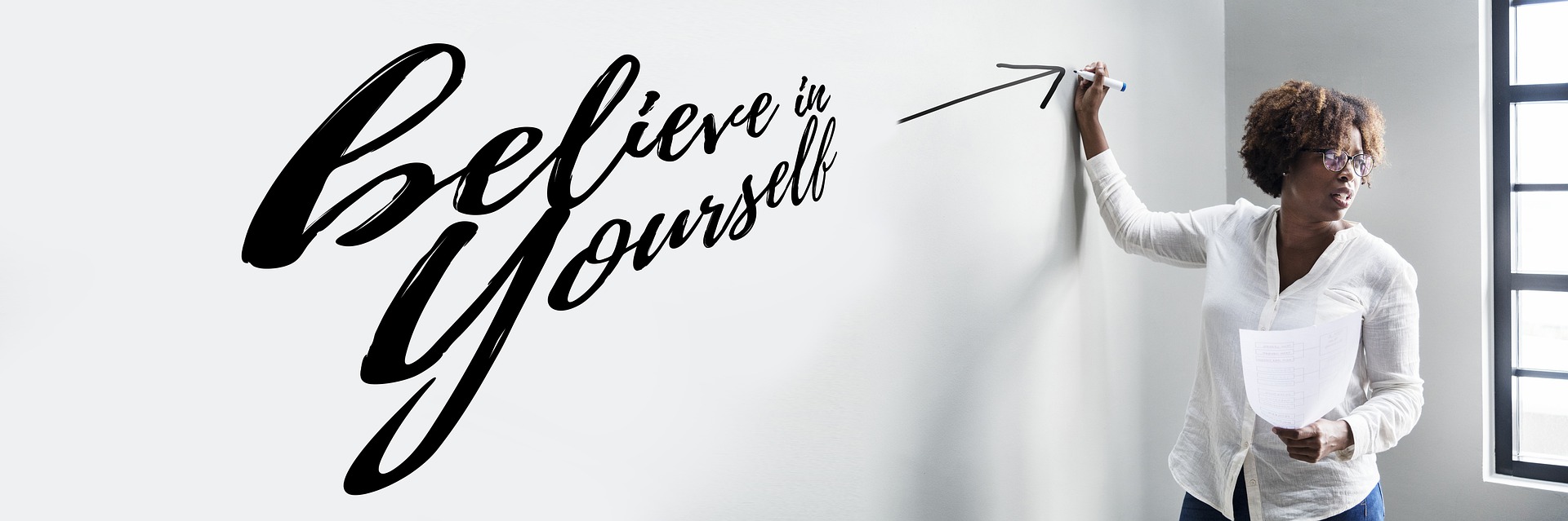 At a presentation, a black woman has written on a whiteboard 'Believe in Yourself'