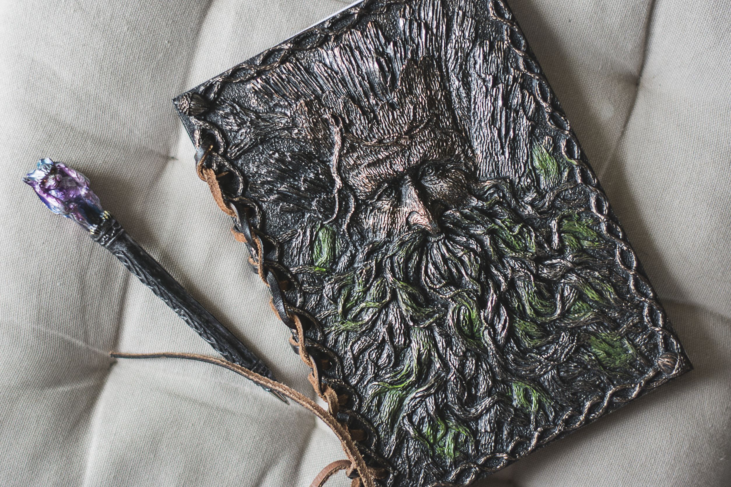 A book with a carved ornate cover featuring the face of an ent. Alongside lies an ornate pen.