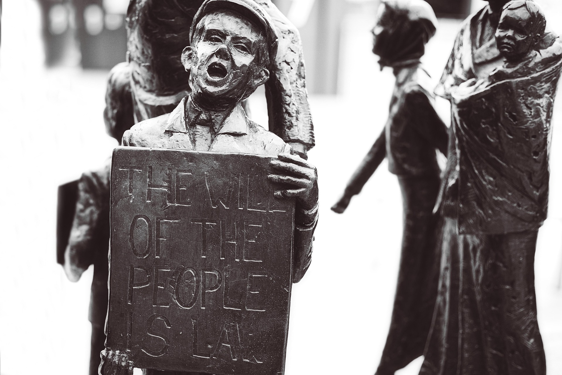 A statue of a boy on a street holding a stone tablet that says, "The Will of the People is Law". He is shouting out to those around.