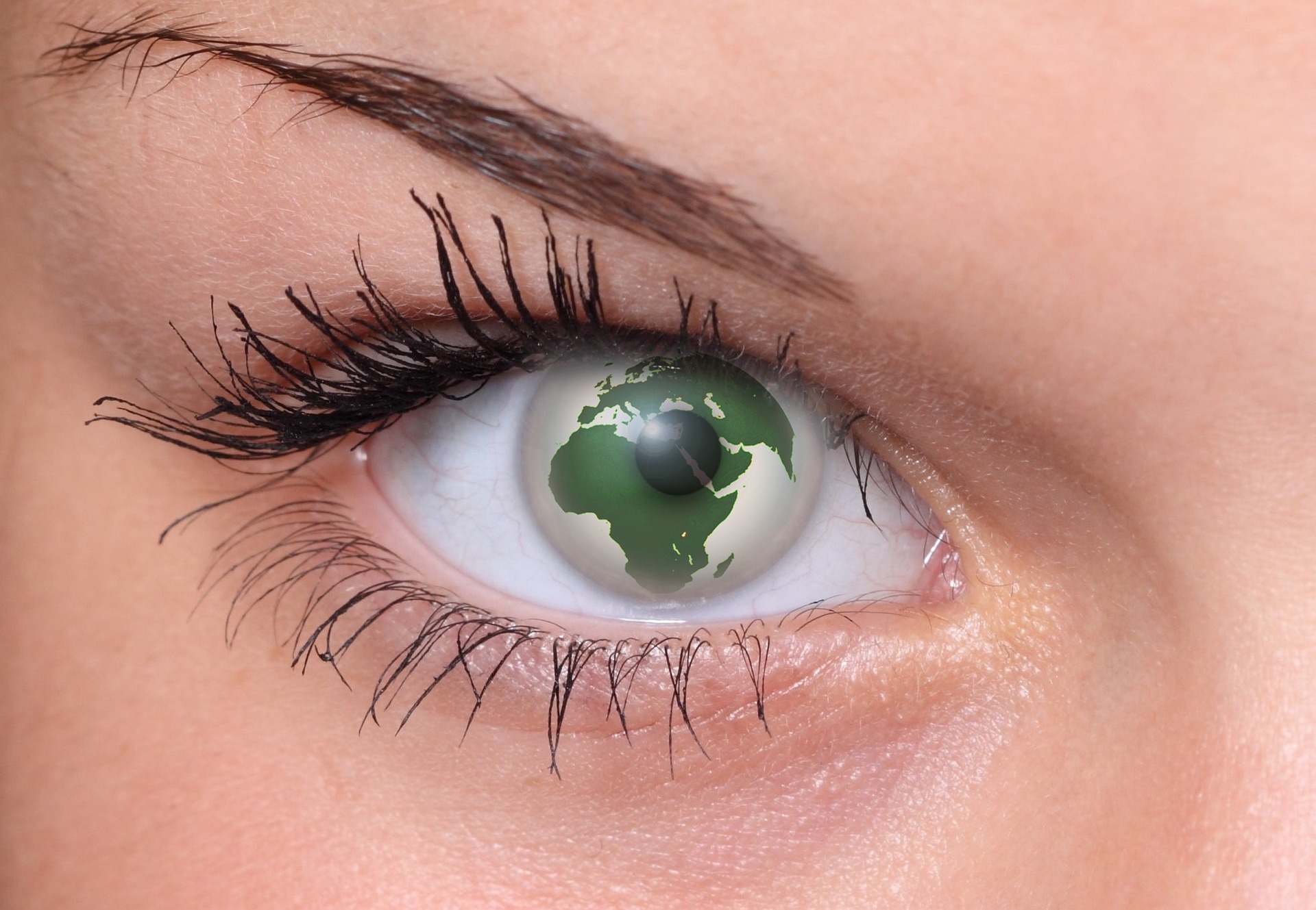A close-up of a woman's eye. The iris is a green planet Earth. There is is also a dark central pupil. The pupil is small and translucent.