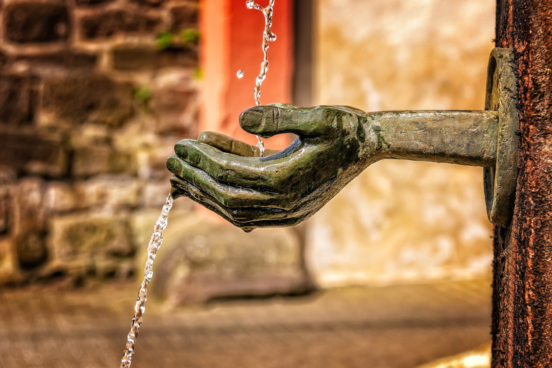 A water feature where a flow of water from above lands in sculpted hands. The water then changes direction and flows onwards.