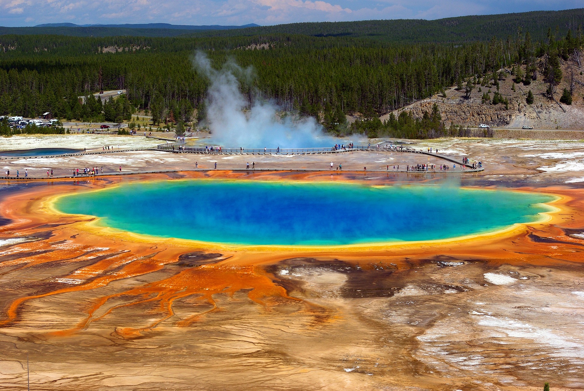 A photo of the multi-coloured Grand Prismatic Spring in Yellowstone National Park in the USA. It is the largest hot spring in the United States and the third largest in the world. The centre and most of it is bluish; the edges have green, yellow, orange, red.