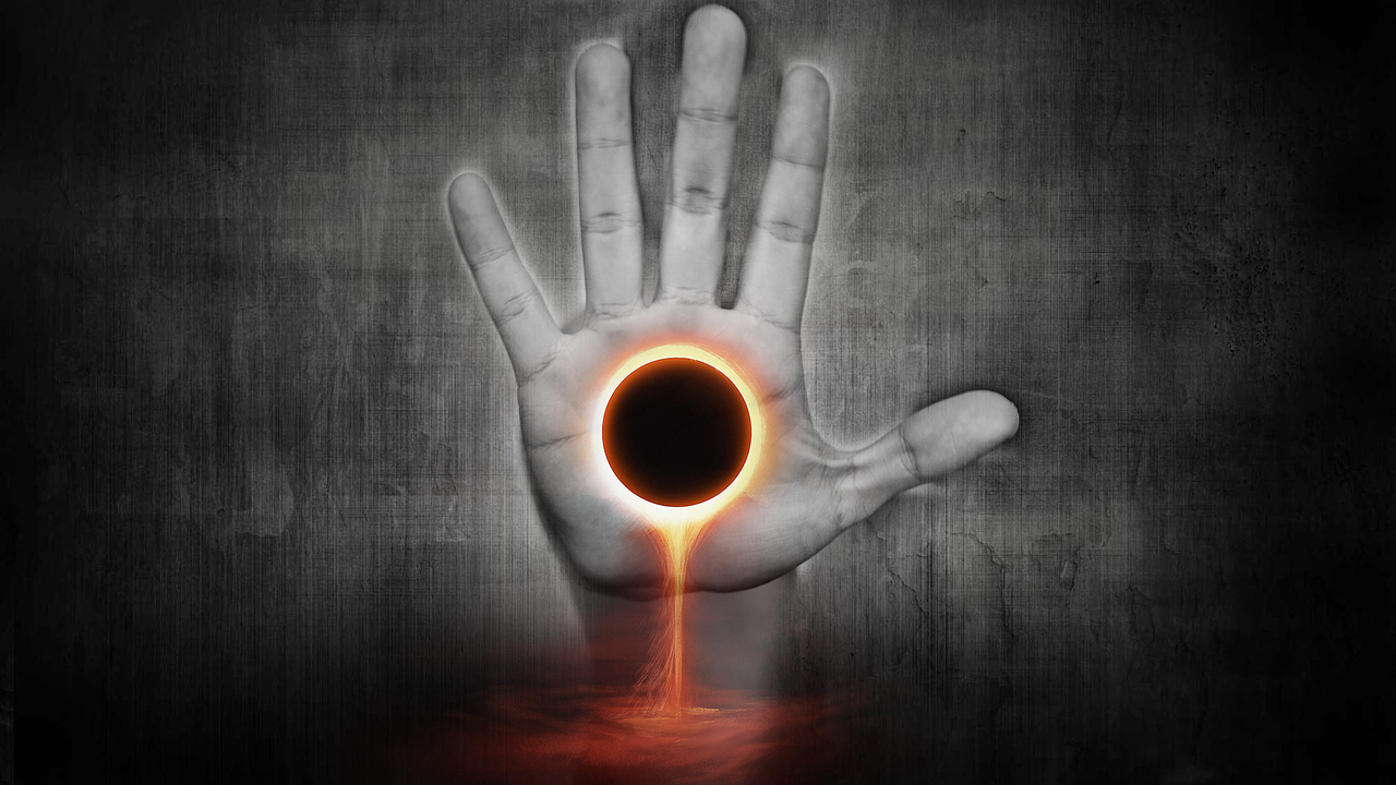Against a dark/grey background, an upright human hand. The palm of the hand has superimposed on it an eclipsed sun. Fire is visible at the edge of the eclipse. Fire leaks downwards.