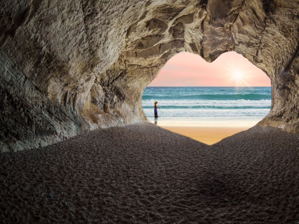 Heart-shaped cave looking out onto sunny beach and ocean