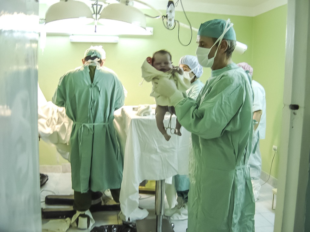 Baby just delivered in a hospital operating theatre, held aloft by a surgeon
