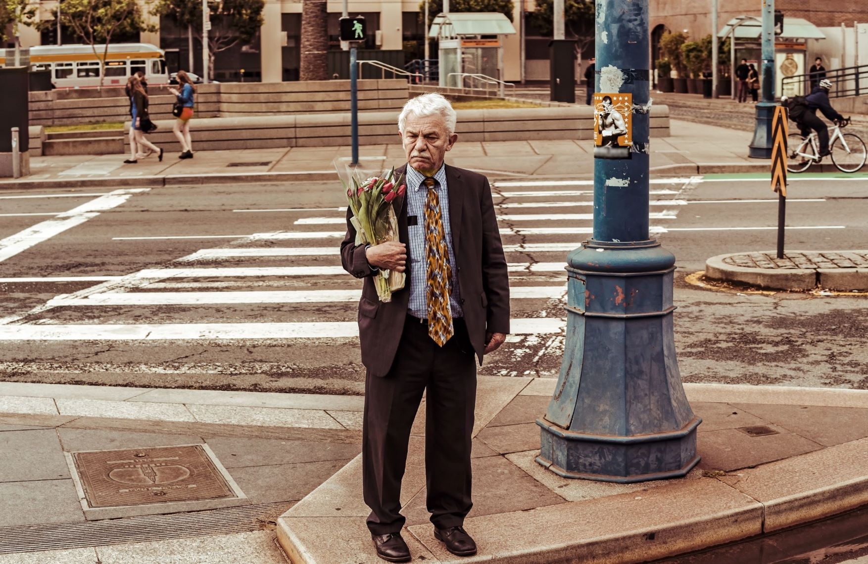 Old man carrying flowers at the kerb of a street, aware of the people nearby, applying allyship