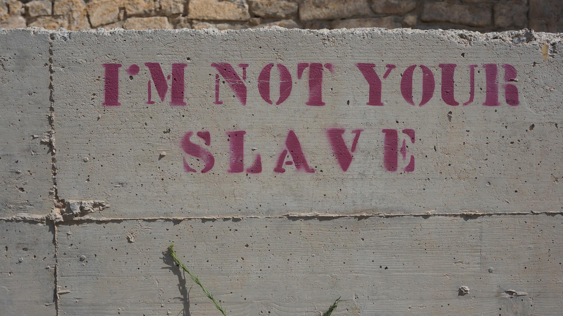 Graffiti print on a concrete wall says in bold pink, "I'm Not Your Slave"
