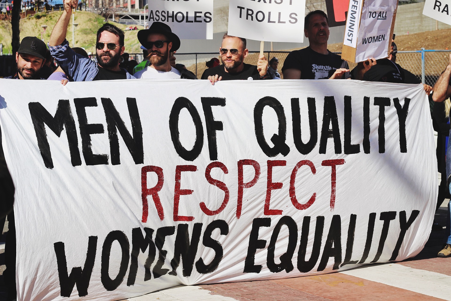 A group of male protesters behind a banner that says 'Men of Quality respect Women's Equality'