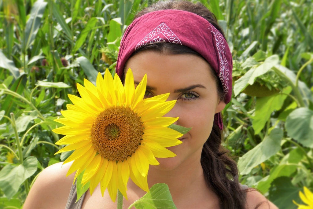 Young woman in a field, her smiling face partially hidden by a sunflower