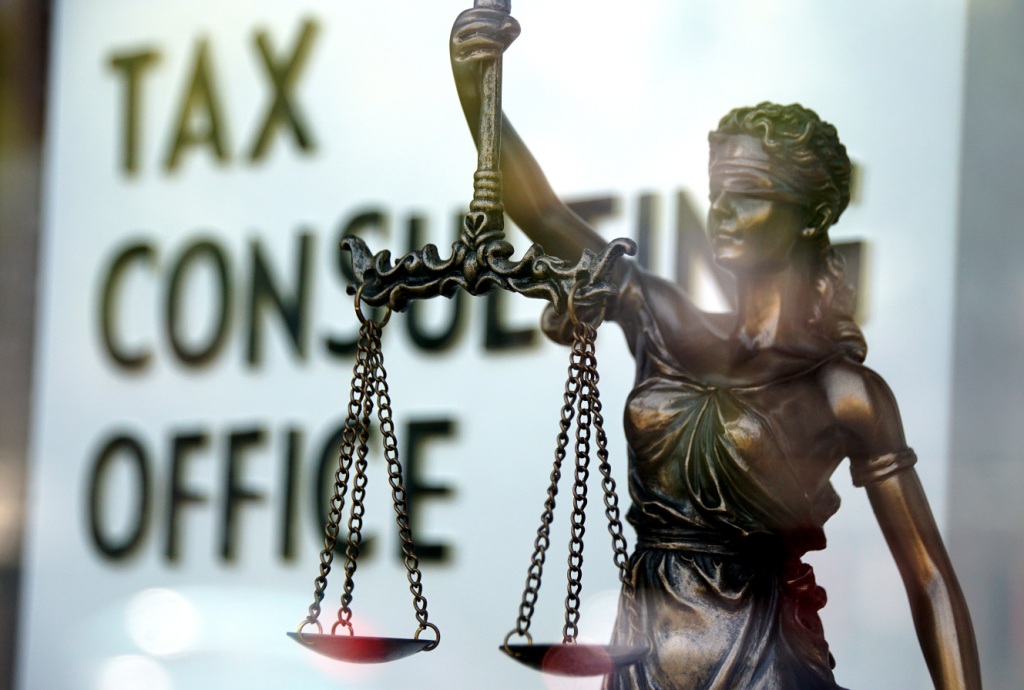 Metal statue of Lady Justice, blindfold, holding a pair of scales, and behind a sign saying 'Tax Consulting Office'