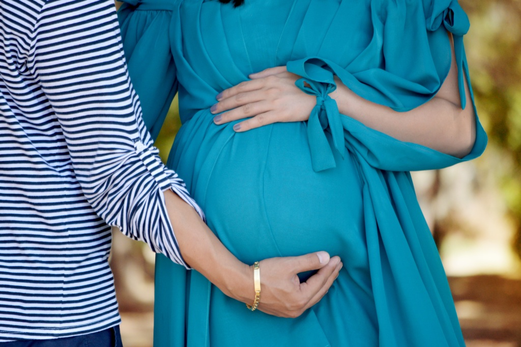 Pregnant mum in blue dress with another, both with hand on her belly