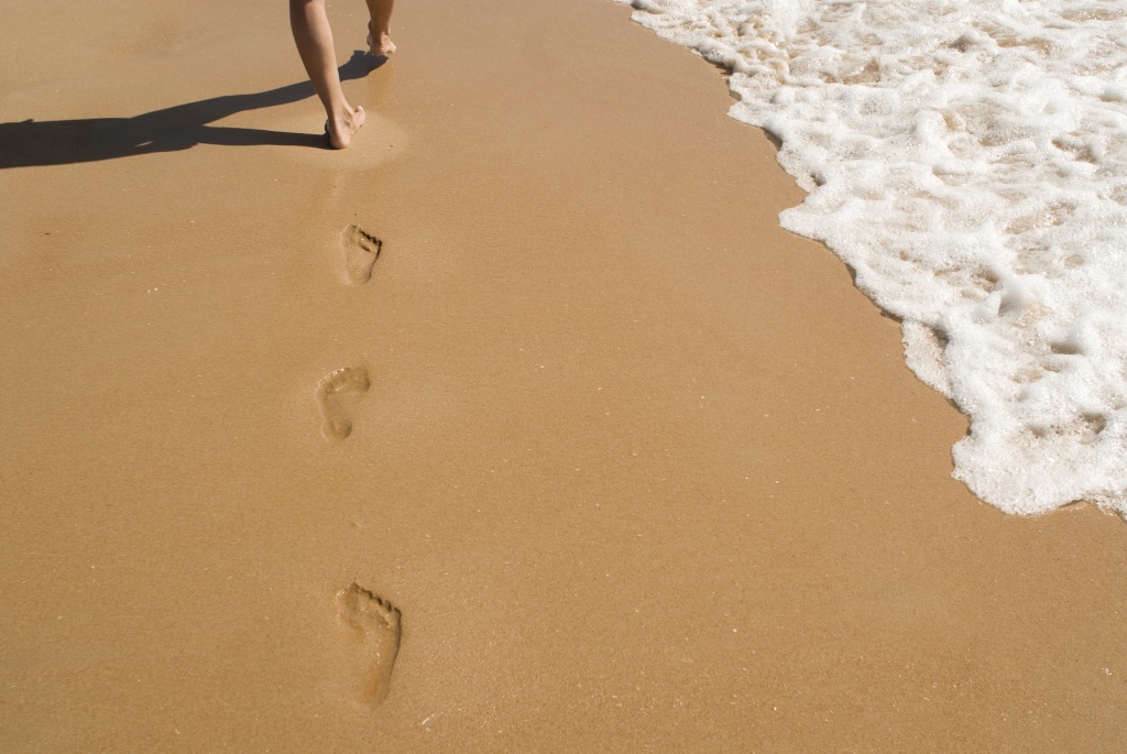 Feet leave footprints where sea and beach meet
