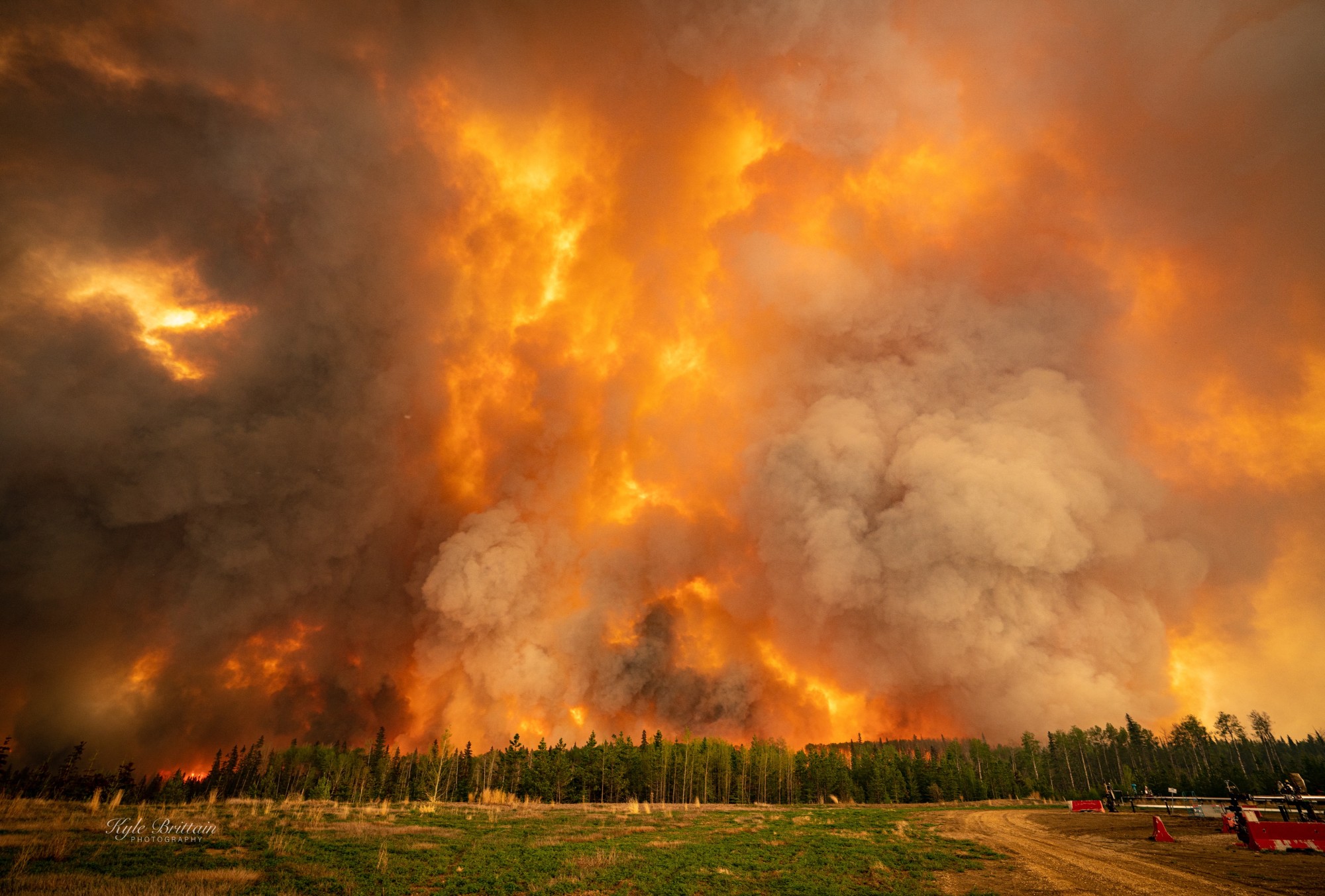 A massive wall of fire and smoke is maybe 15 to 20 times higher than the tall coniferous trees