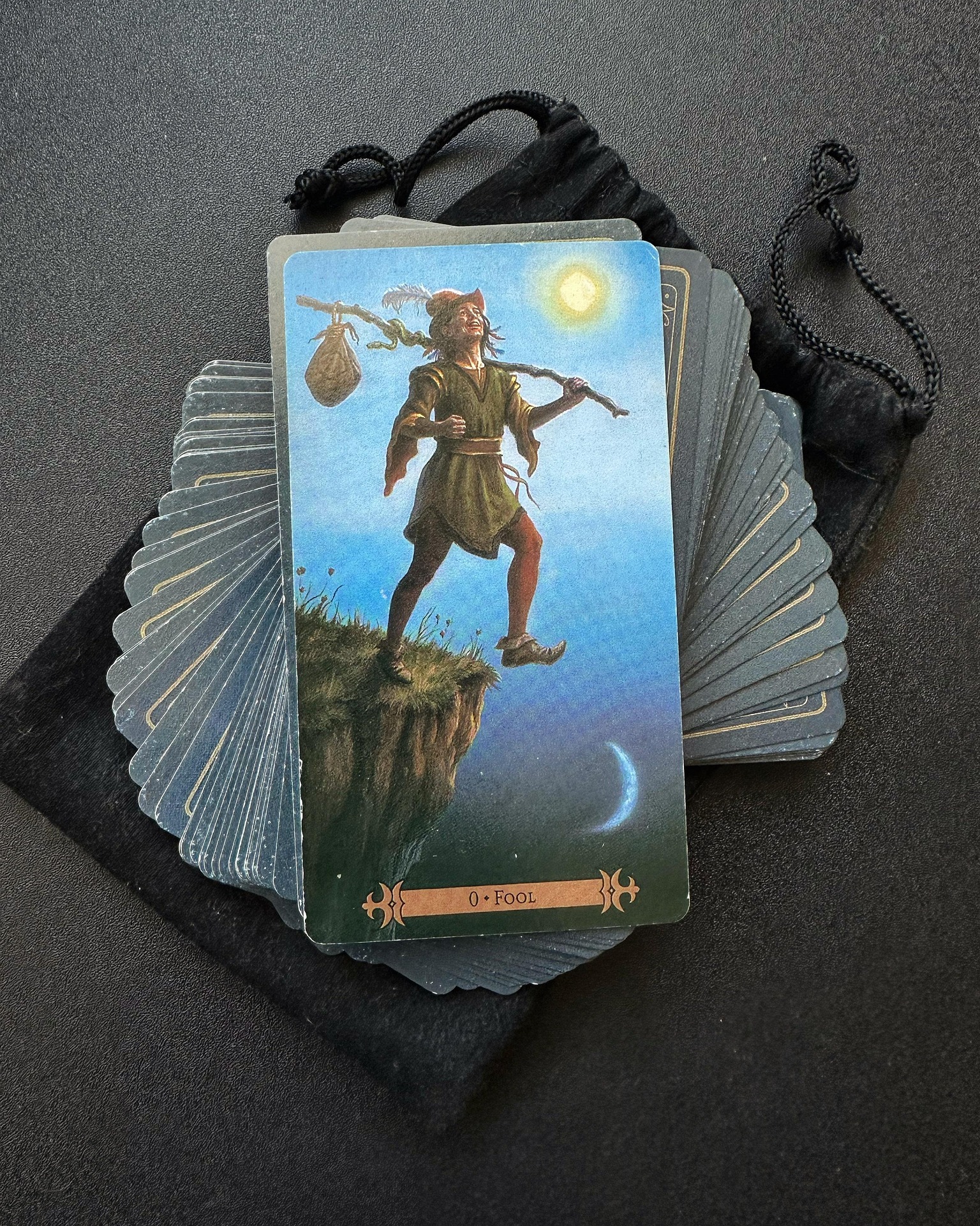 A pack of Tarot cards and its bag are in an artistic pile, with The Fool card on top