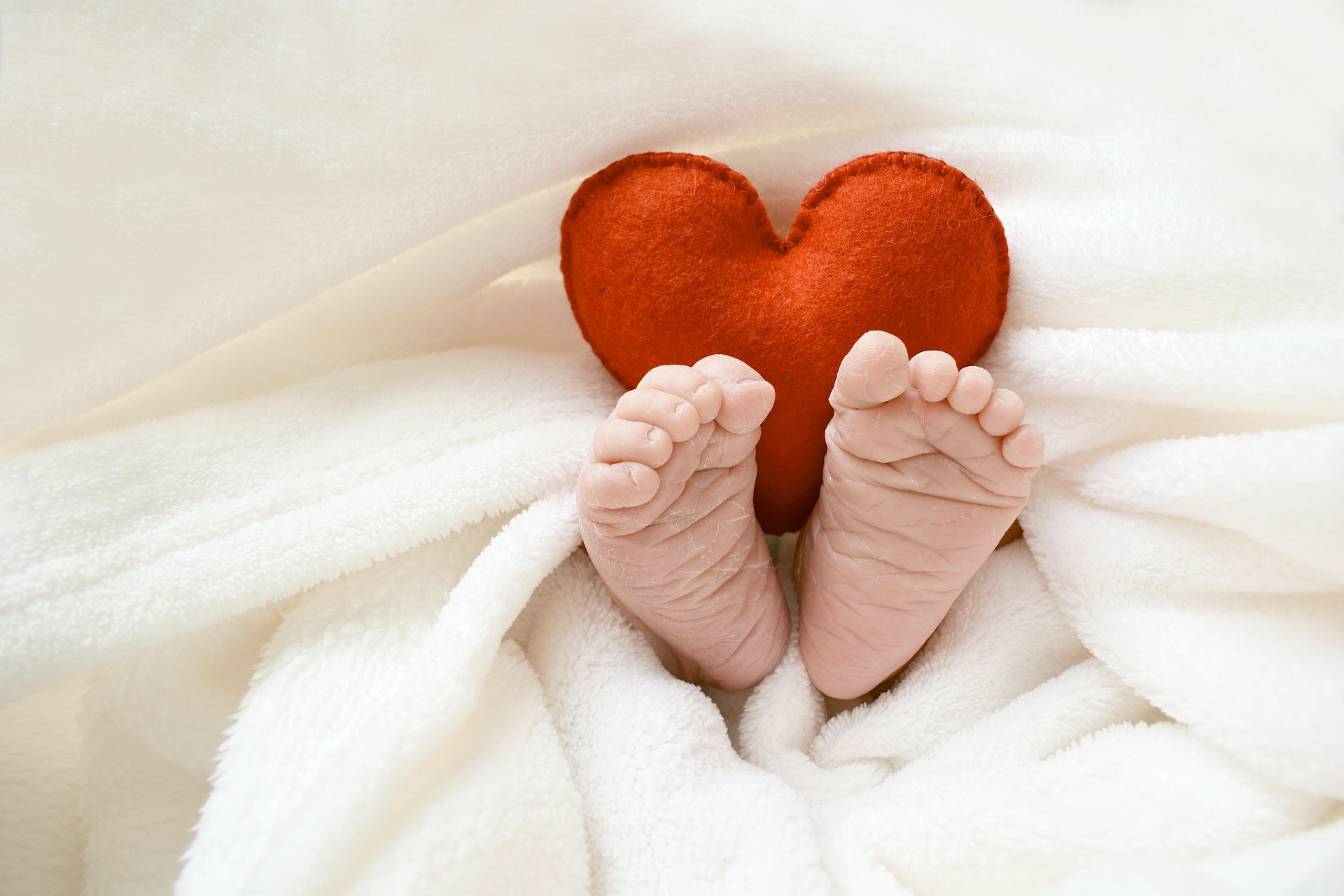 Baby feet and a small heart cushion stick out from some bedding - very cute!