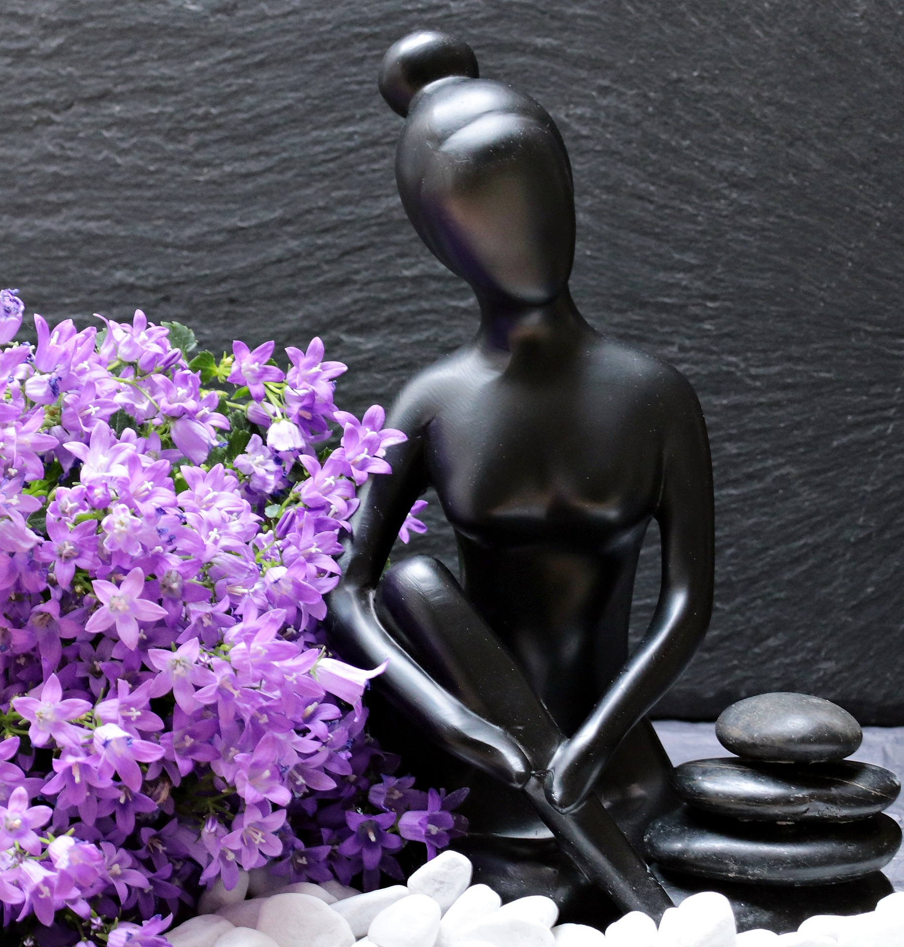 A statue of a beautiful black woman, sitting cross-legged, by fragrant flowers and small stones