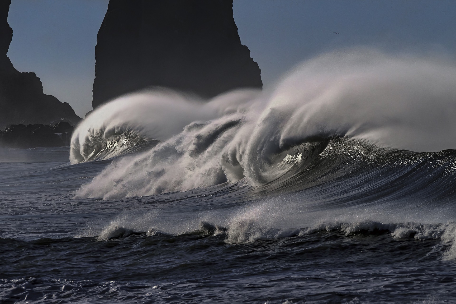 Vigorous waves roll into the shore, creating beautiful curving sprays above them