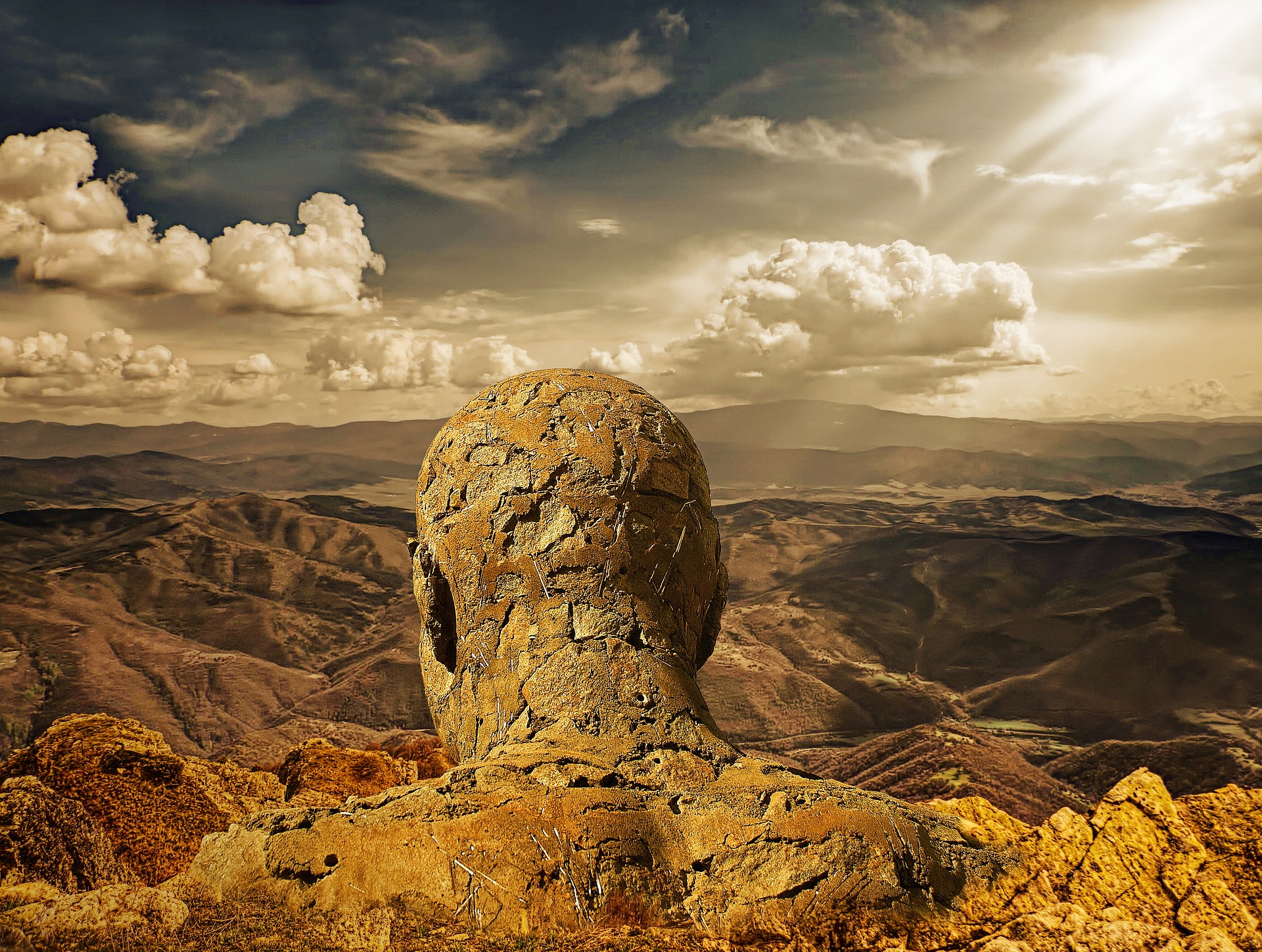From a mountain landscape emerges the head and shoulders of a giant stone man